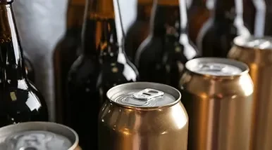 Three golden cans with blurred amber glass bottles in the background.