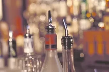 Two liquor bottles with metal pour spouts in a dim bar.
