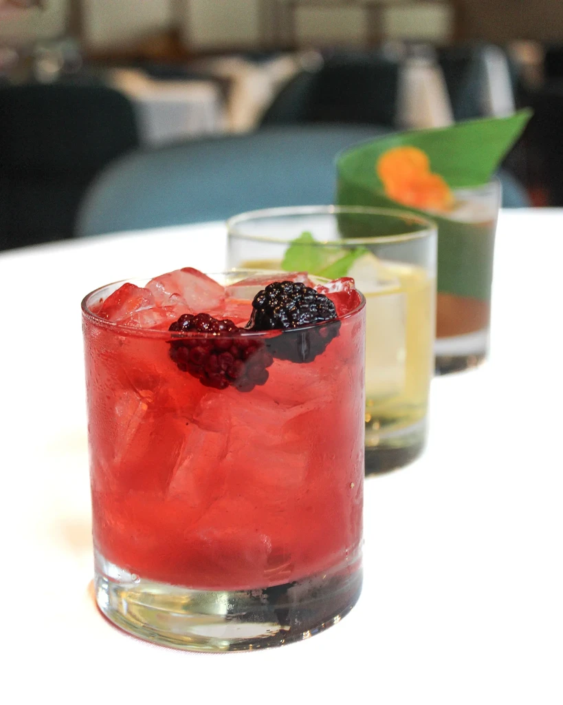Three colorful drinks: red, yellow, and layered, with ice and garnishes.