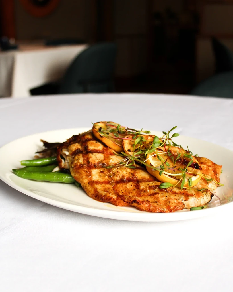 Grilled protein with lemon, microgreens, and green beans plated in a restaurant.