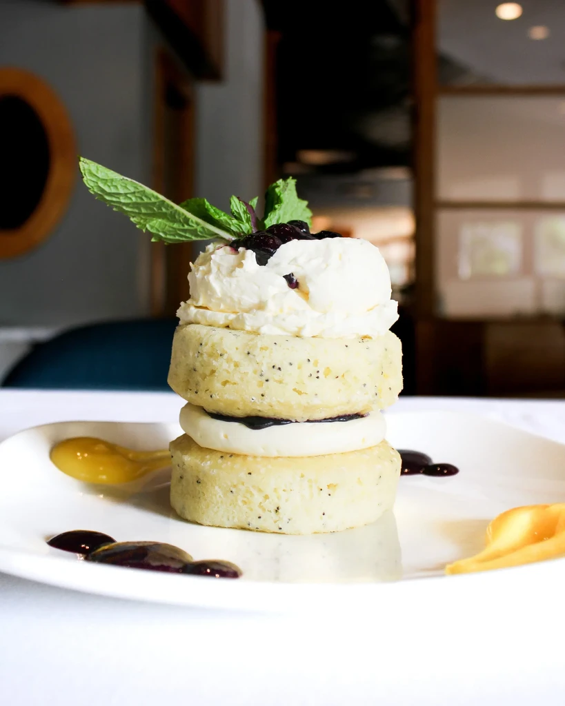 Stacked poppy seed cakes with berry sauce, cream, and mint.