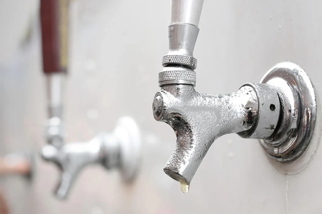 Close-up of a chrome beverage tap with condensation and a liquid drop.