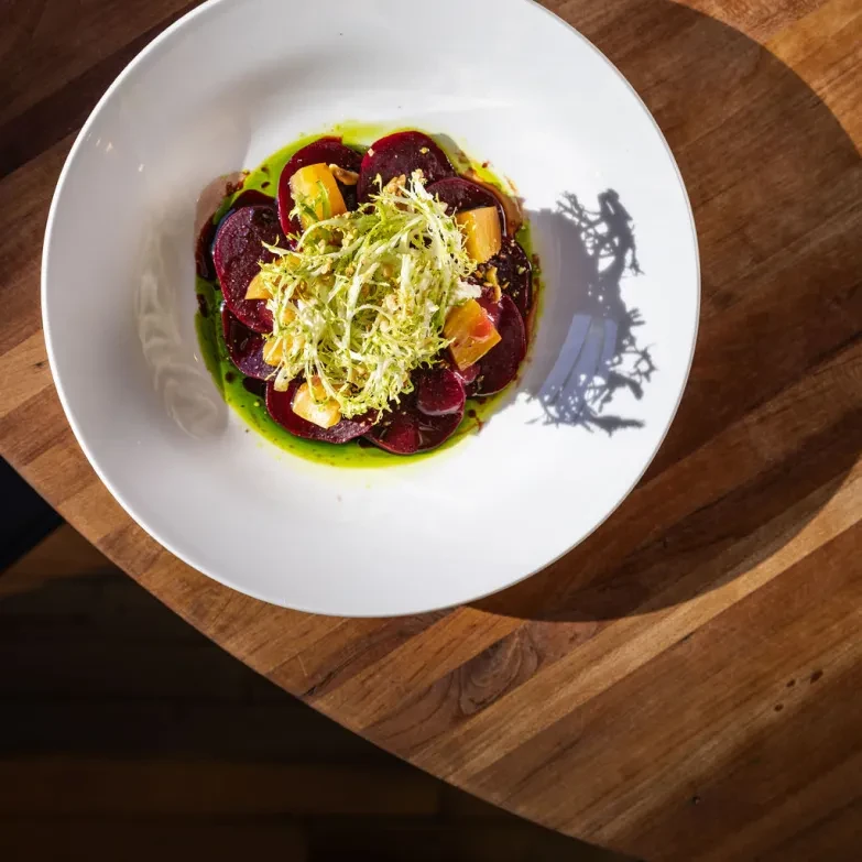 Beetroot and frisée salad with green dressing, intricate shadow on wood table.