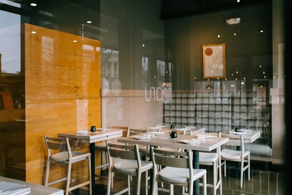Empty, modern restaurant interior with tables, art, and reflective window view.