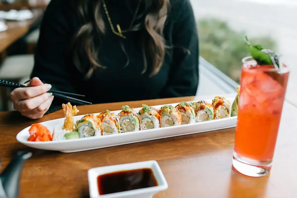 Person using chopsticks to pick up sushi next to a red drink.