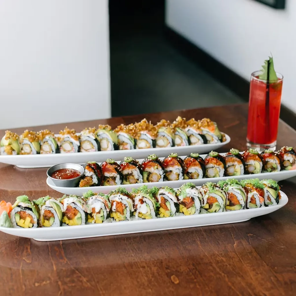 Three platters of diverse sushi rolls and a pink drink on a wooden table.