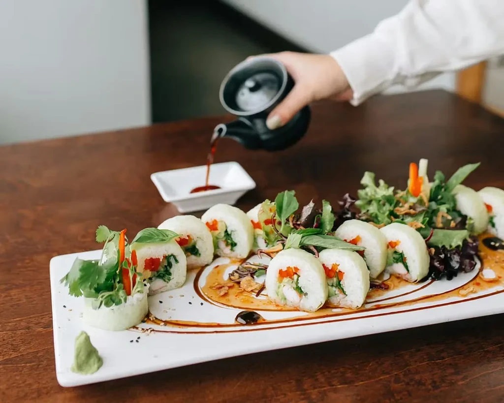 Plated green rolls with shrimp, vegetables, herbs, sauce, and wasabi.