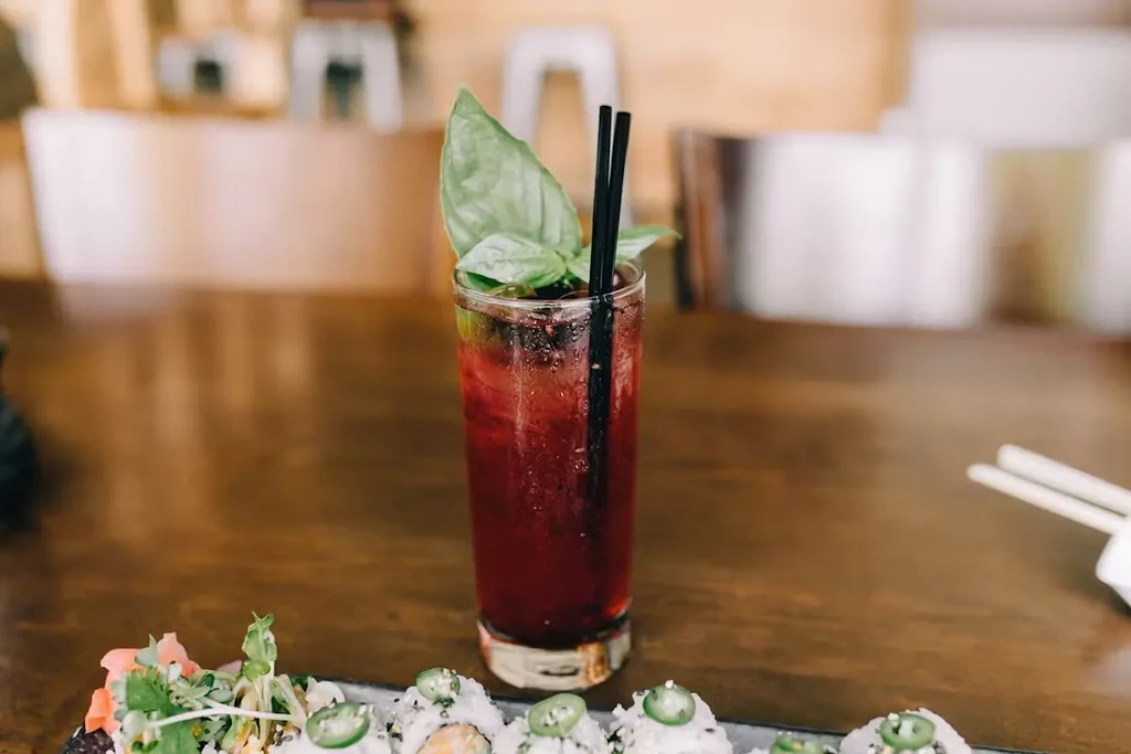 Basil-garnished purple drink and sushi rolls on a wood table.
