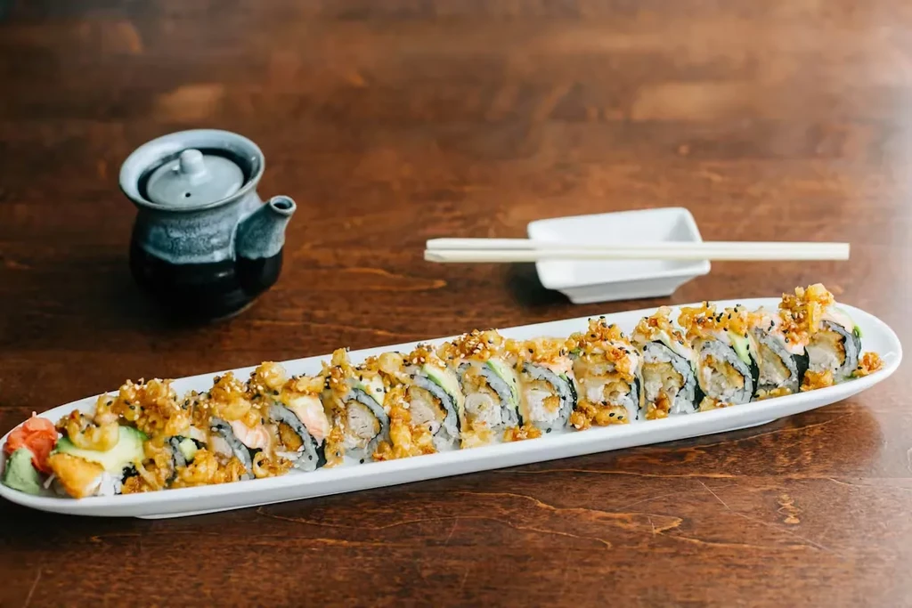 White plate of crispy tempura sushi rolls with ginger and wasabi.