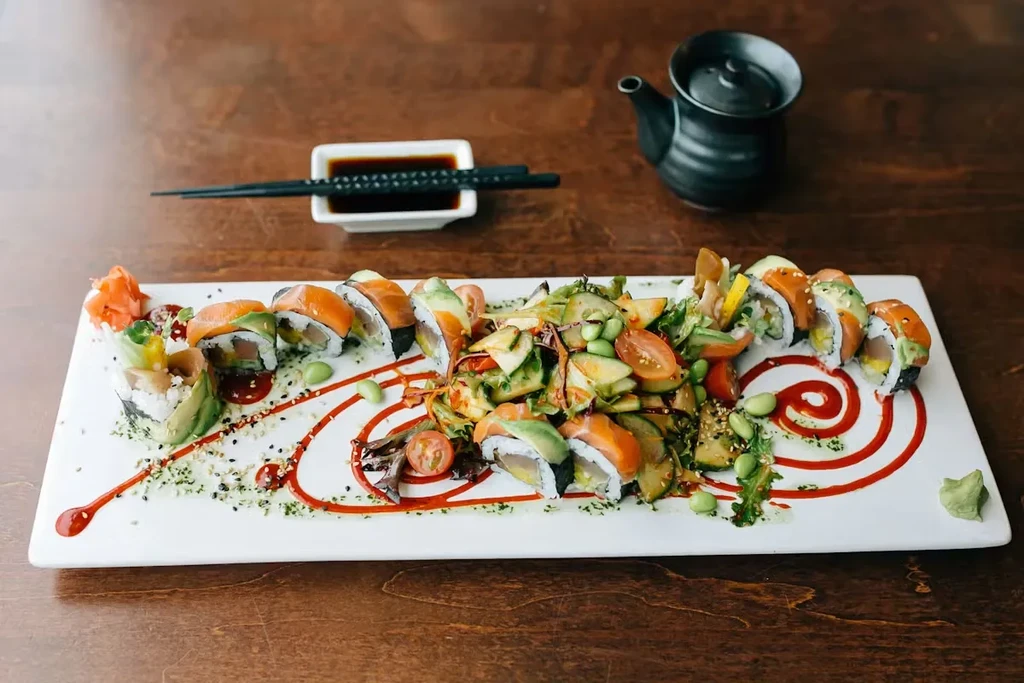 Plated sushi rolls, salad, teapot, soy sauce, and chopsticks.