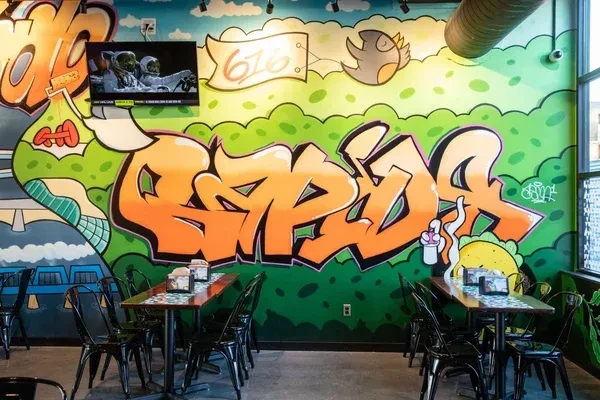 Colorful graffiti mural covers restaurant wall above dining tables.