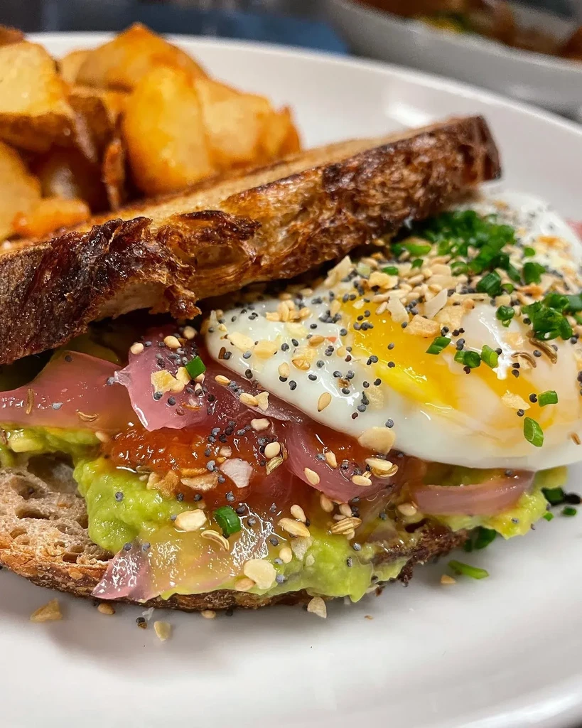 Avocado toast with fried egg, runny yolk, pickled onion, and potato wedges.