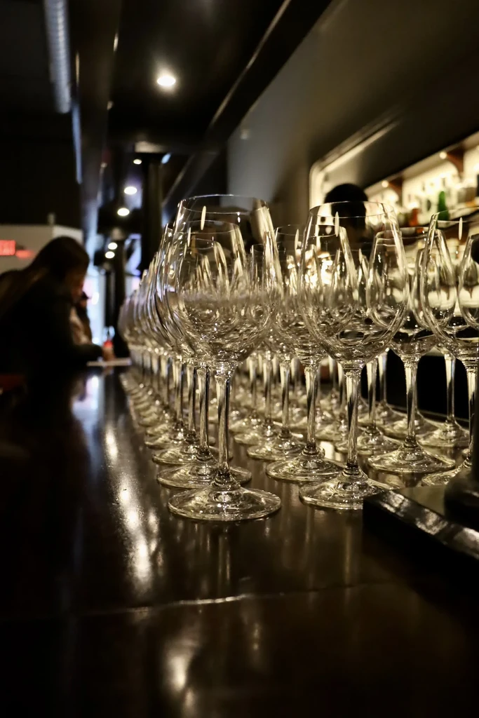 A long row of empty wine glasses on a dark, reflective bar.