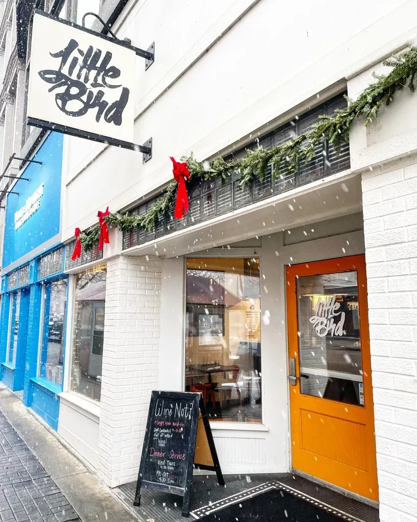 Snowy Little Bird restaurant exterior with orange door and holiday garland.