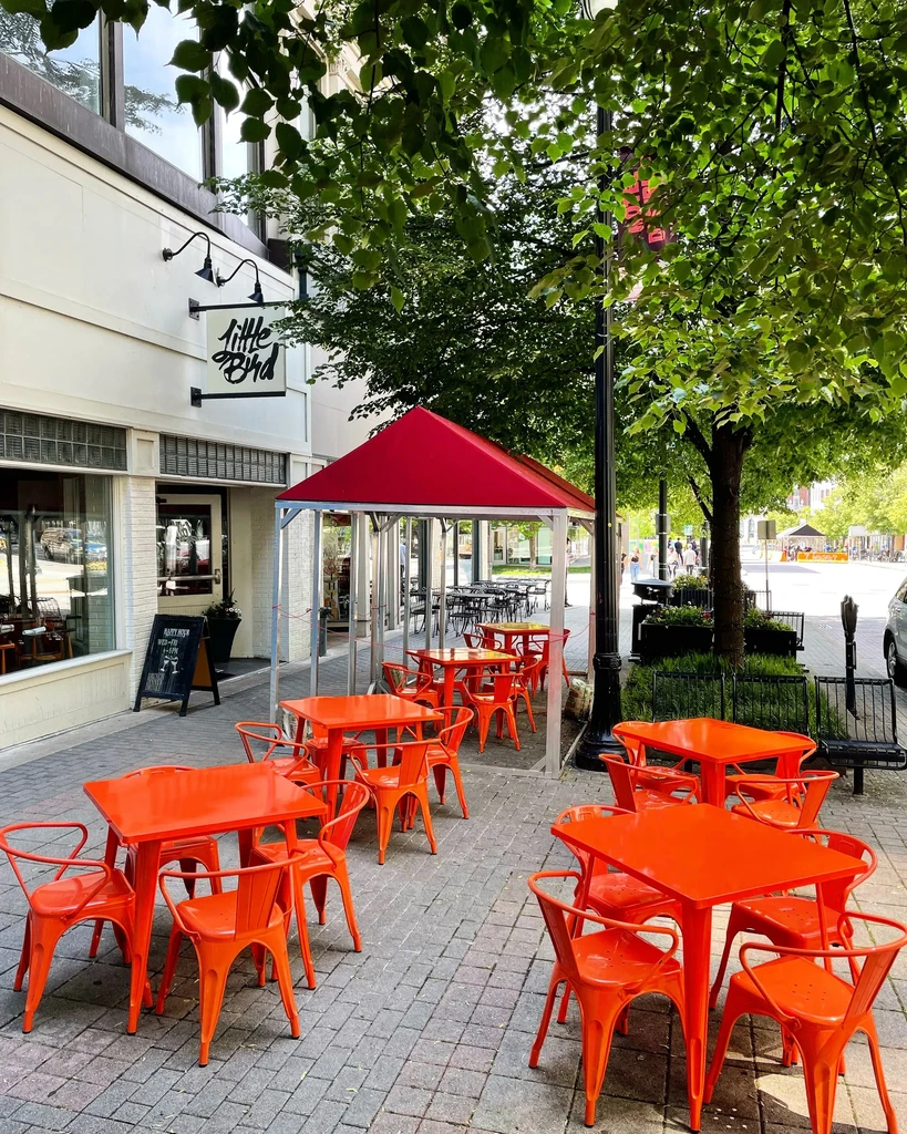 Little Bird restaurant's outdoor seating with orange tables, chairs, and red canopy.