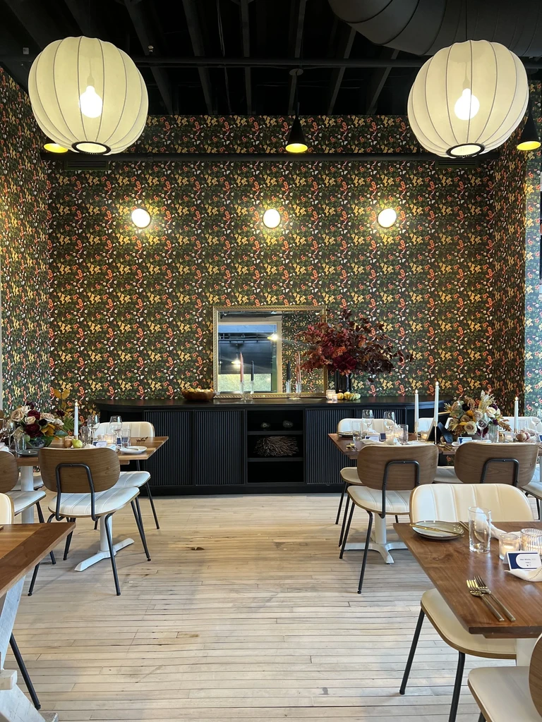 Stylish restaurant dining room with dark floral wallpaper and warm lighting.