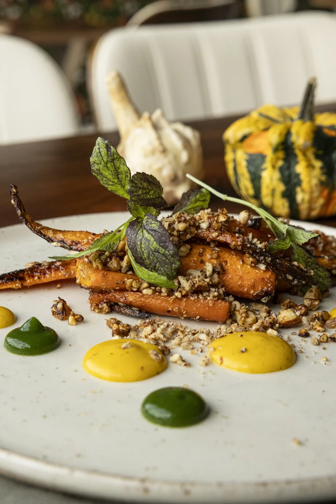 Roasted carrots garnished with nuts, herbs, and green and yellow sauces.