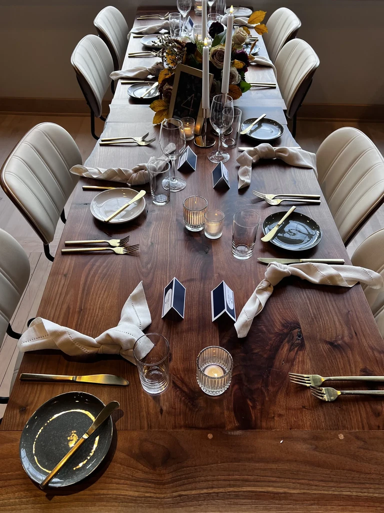 Long wooden table set with autumnal floral centerpiece, candles, and place settings.