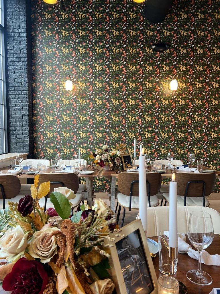 Long dining table with flowers and candles against green floral wallpaper.