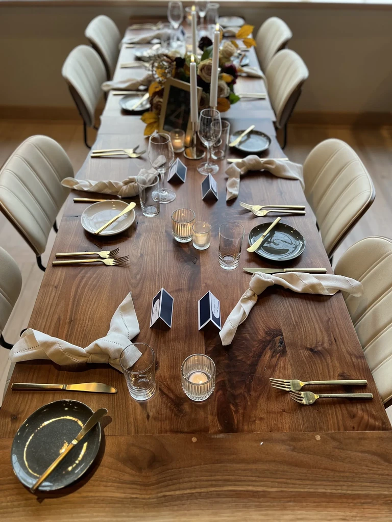 Long wooden dining table set with autumnal centerpiece, candles, and place settings.