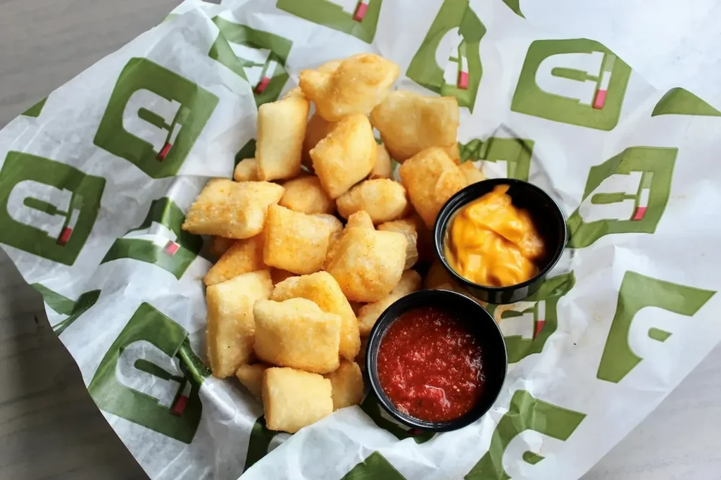 Golden-brown fried dough pieces with orange cheese and red sauces.