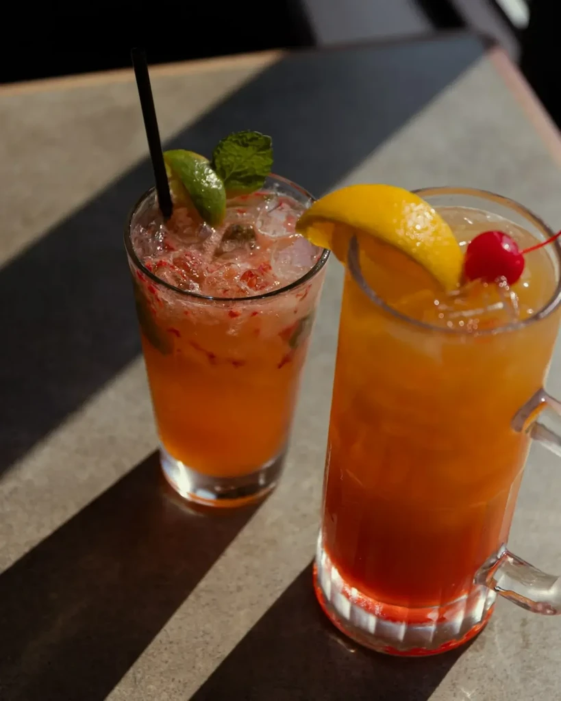 Two colorful, refreshing cocktails with fruit garnishes on a sunny table.