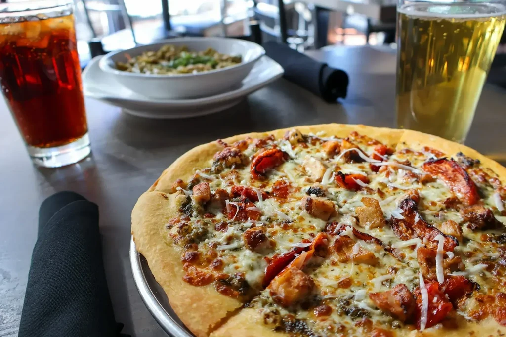 Close-up of a pizza with meat, two drinks, and salad on a restaurant table.