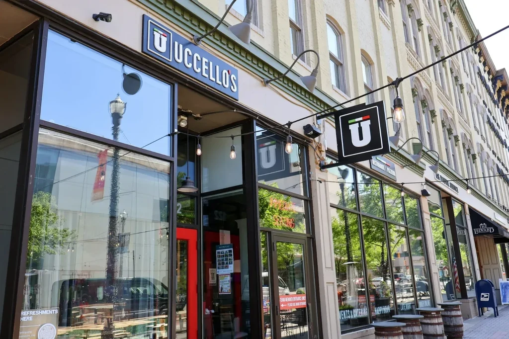 Uccello's restaurant exterior: red door, blue sign, string lights, and barrels.