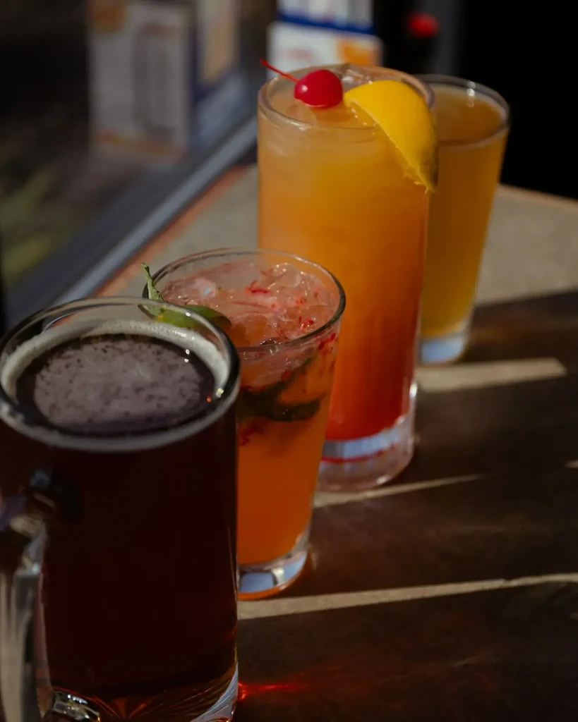 Four diverse drinks, including beer and cocktails, on a dark wood surface.