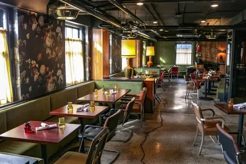 Empty vintage-style restaurant with olive green booth and floral wallpaper.