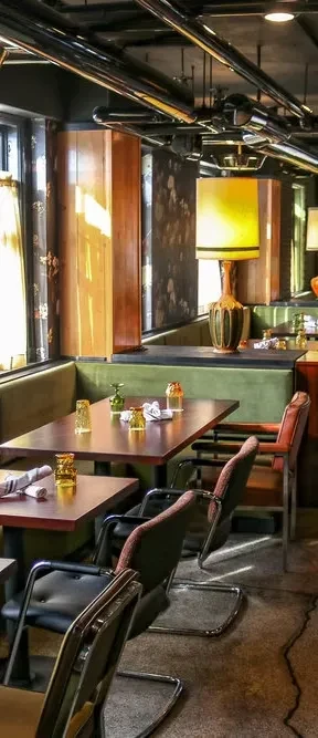 Empty modern-rustic restaurant dining room with olive banquettes and yellow lamp.