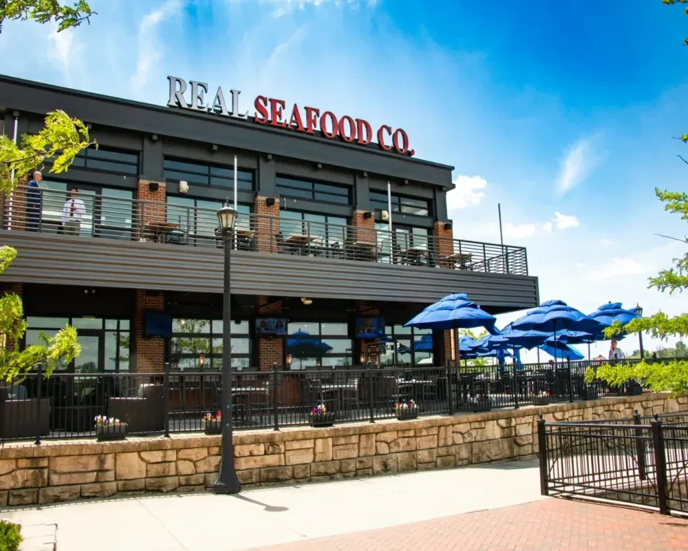 REAL SEAFOOD CO. restaurant exterior with blue umbrellas and outdoor seating.