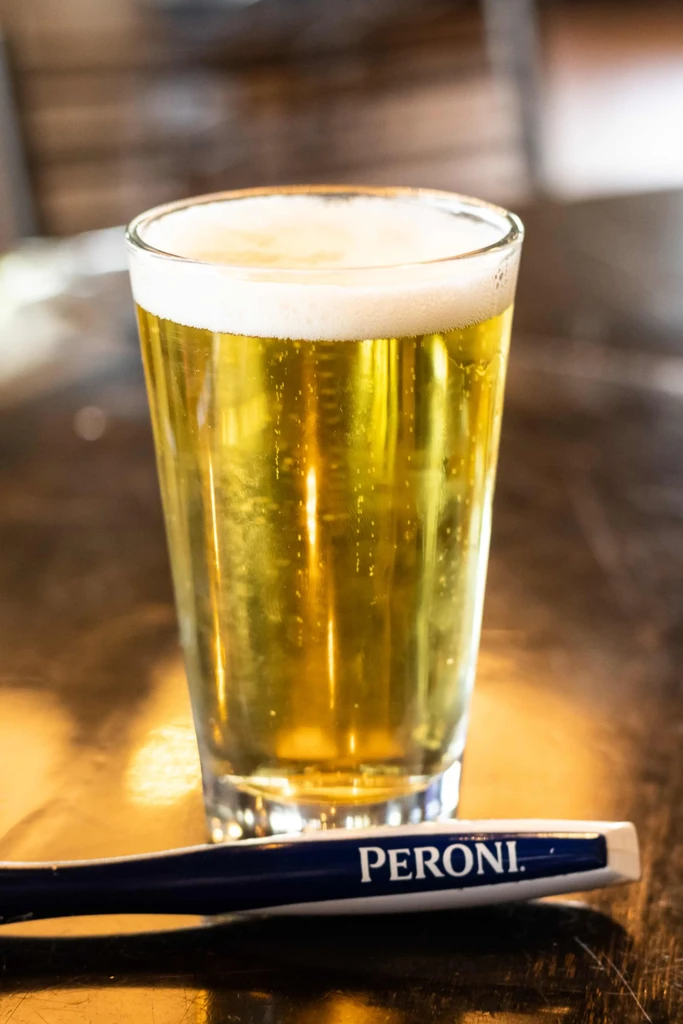 Close-up of a golden beer with frothy head and Peroni branding.