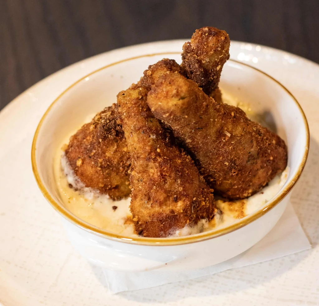 Close-up: Four fried food pieces in creamy sauce, white bowl.