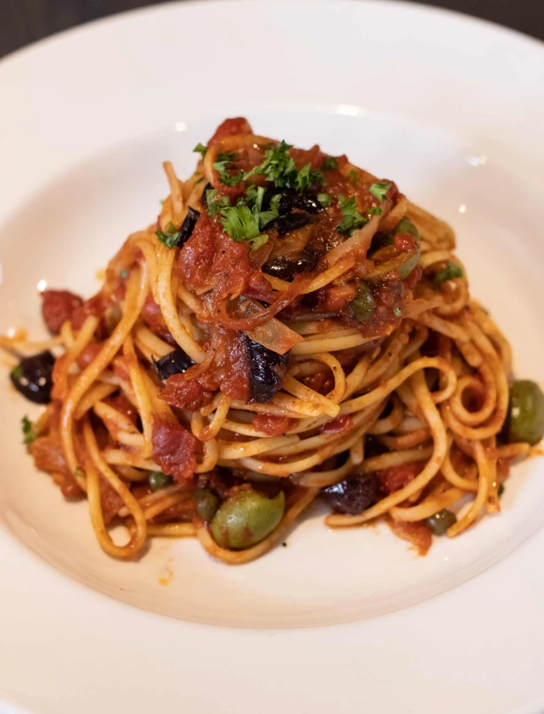 Well-plated pasta with tomato-olive sauce and green herbs.