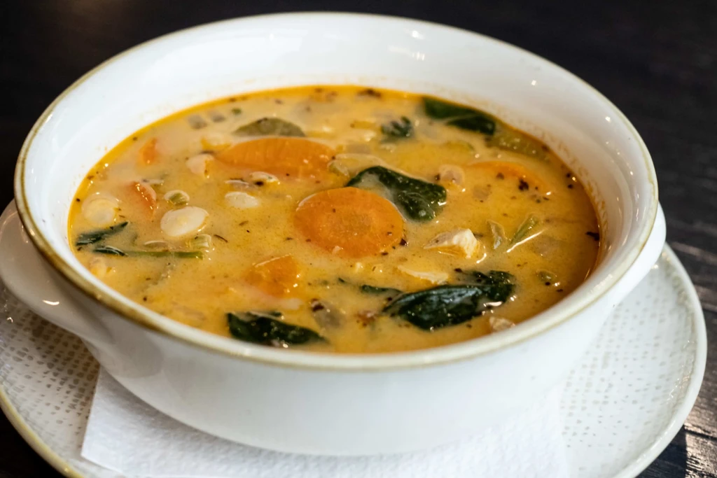 Close-up of hearty orange-yellow soup with carrots, greens, and white pieces.
