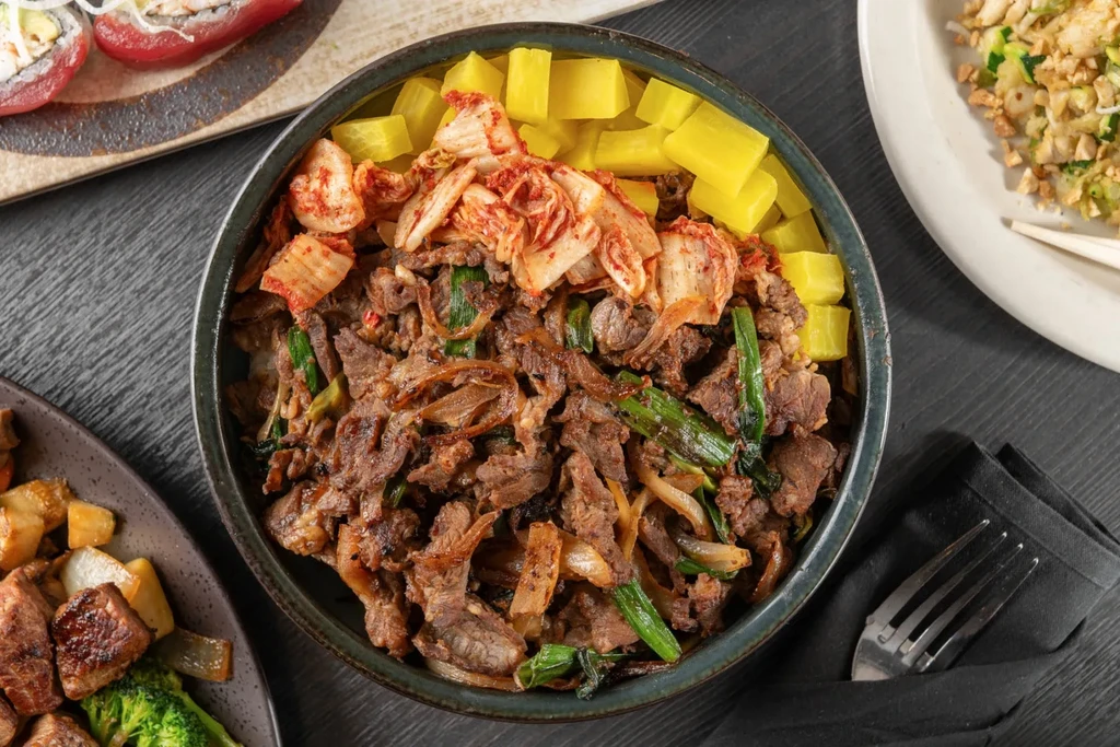 Overhead shot of bulgogi-style rice bowl surrounded by other Asian dishes.