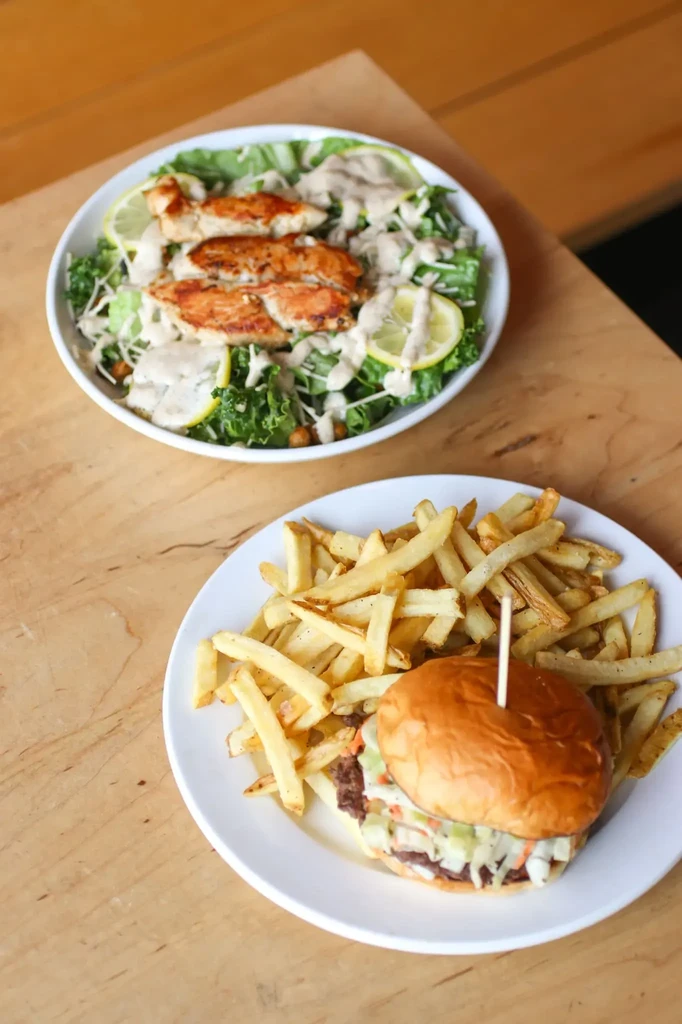 Burger with fries and a grilled chicken salad on a table.