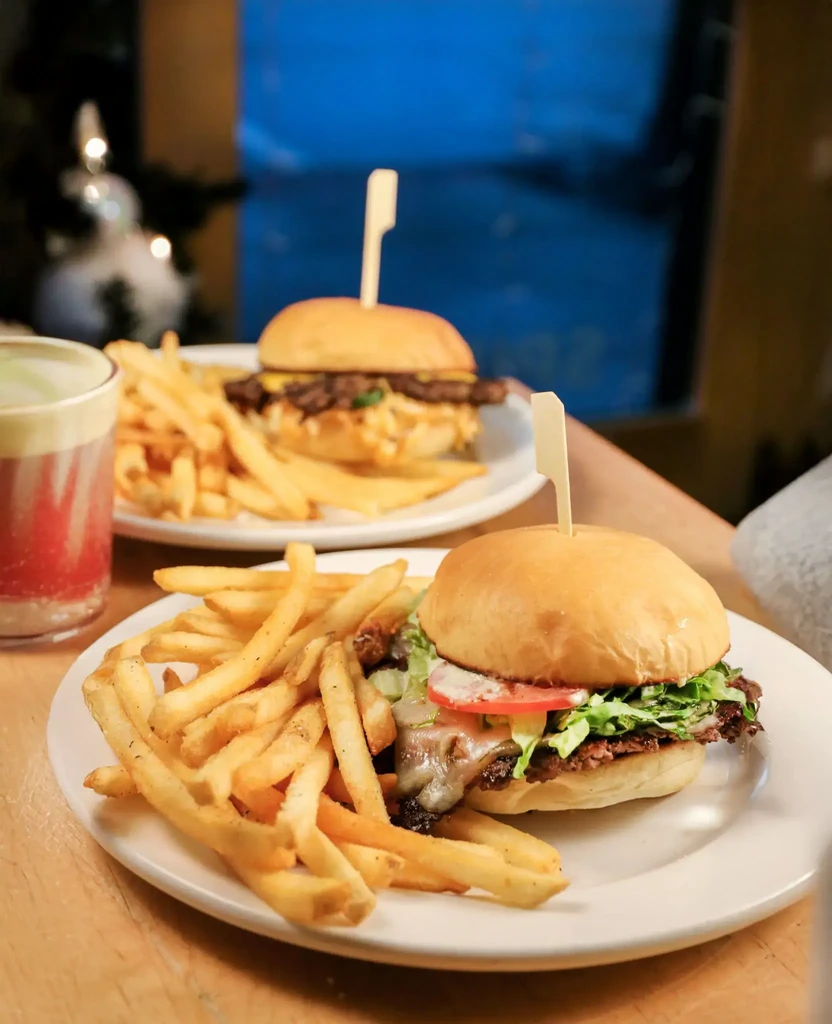 Plates of burgers and golden fries at a restaurant with festive lights.