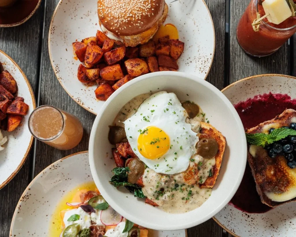 Overhead photo of a brunch spread: burger, French toast, egg dish, and drinks.