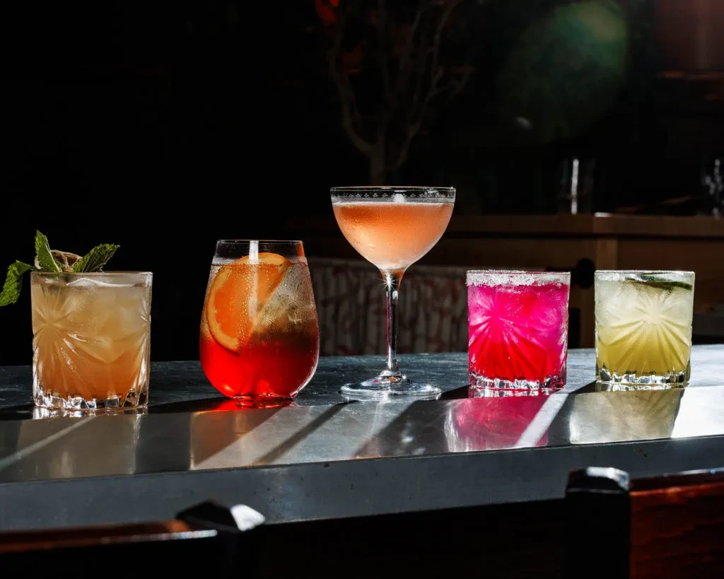Five distinct, garnished cocktails arranged on a sleek bar counter.