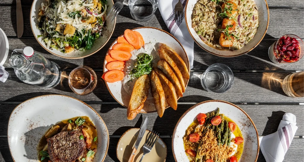 Flat lay of rustic table set with five gourmet meals and drinks.