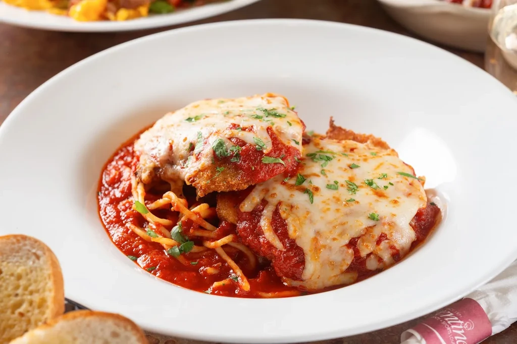 Chicken Parmesan in bowl with spaghetti, garlic bread, and Santino's logo.