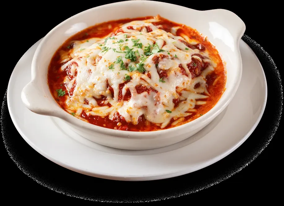 Baked pasta in white oval dish with red sauce, melted mozzarella, herbs.