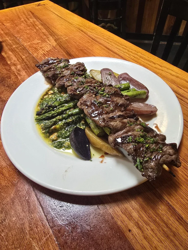 Grilled steak skewers, green asparagus with sauce, and roasted potatoes.