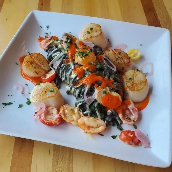 Dark pasta with shrimp, seared scallops, tomatoes, and green herbs.