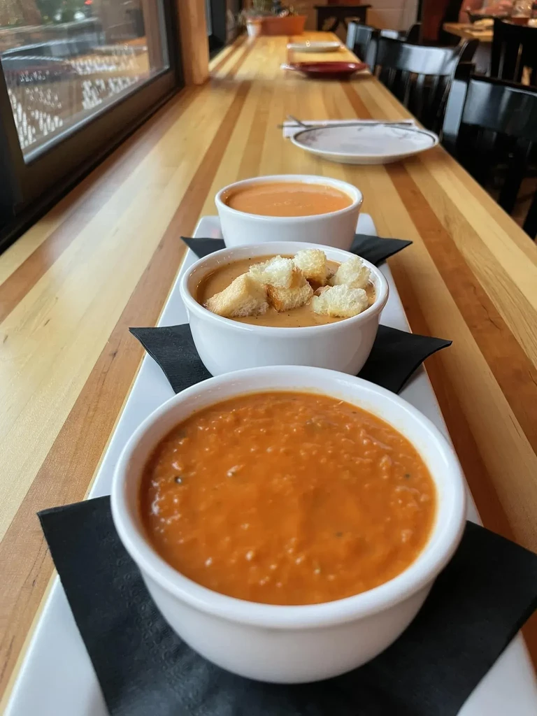 Three bowls of creamy red soup with croutons in a restaurant.