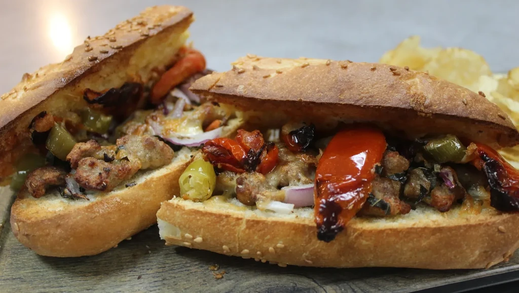Two open-faced baguette subs with meat, peppers, and onions.