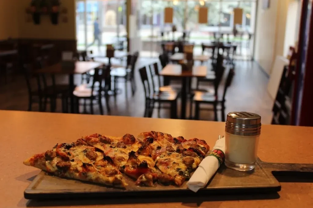 Partially eaten pizza on a wooden board with shaker and decorative napkin.