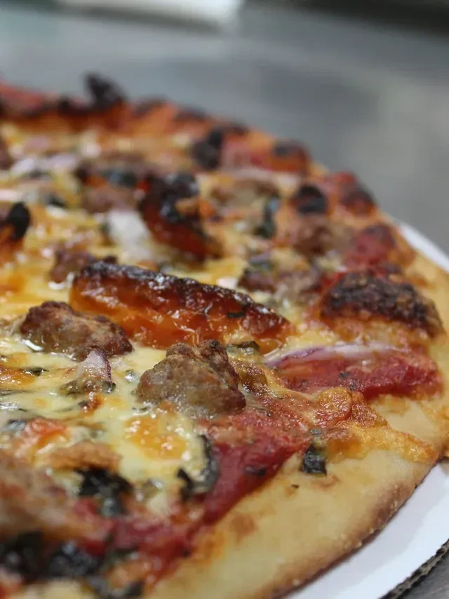 Close-up of pizza with sausage, roasted peppers, red onion, and melted cheese.